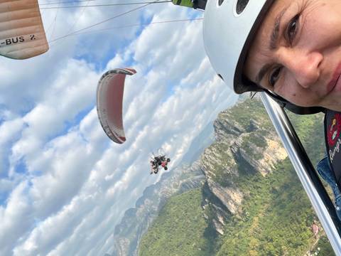 Person paragliding over a mountainous landscape with another paraglider in the distance.