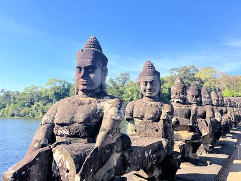       Stone statues lined up with a body of water and trees in the background.
  