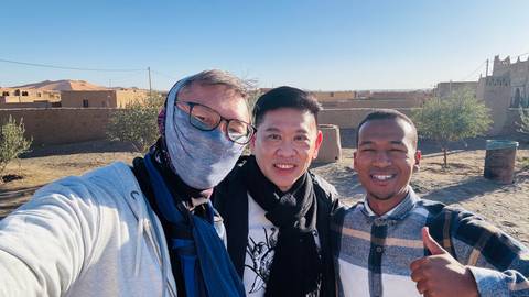 Three people posing in an outdoor setting with sand.