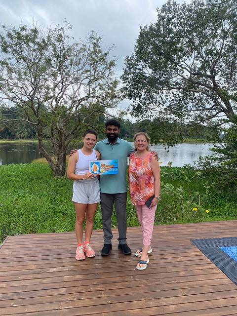 Group of people posing with a 'Mango Vacations' sign by a lake.
