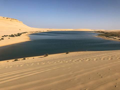       Sandy desert landscape with water body.
  