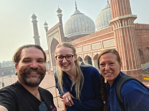 Three people posing in front of a mosque with large domes and minarets.