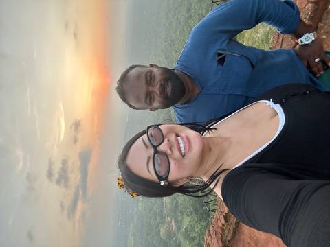 Two people smiling with a sunset and valley in the background.