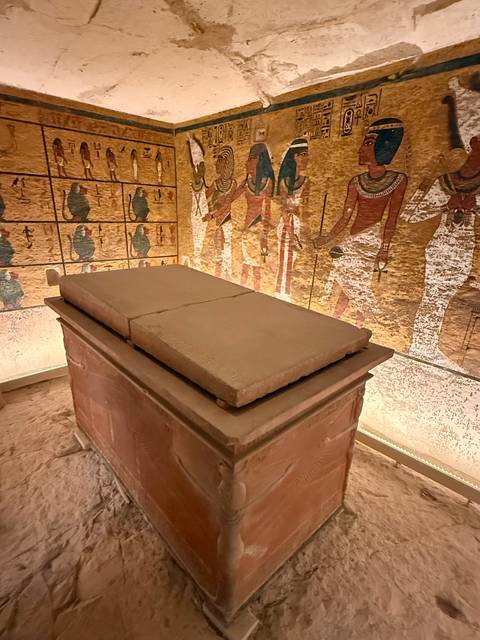      Sarcophagus with ancient Egyptian mural in a museum setting.
  