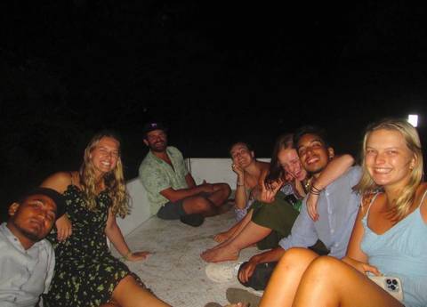 Group of people sitting together at night, some posing and smiling.