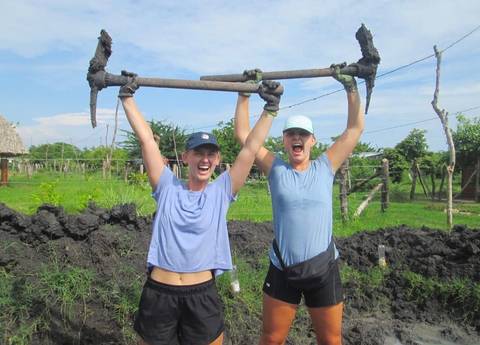 Two women holding up tools in a field, smiling.