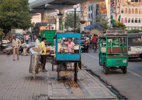      Busy street scene with food vendors and rickshaws.
  