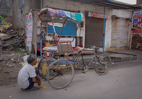 An older man sitting next to a classic rickshaw on an urban street.
