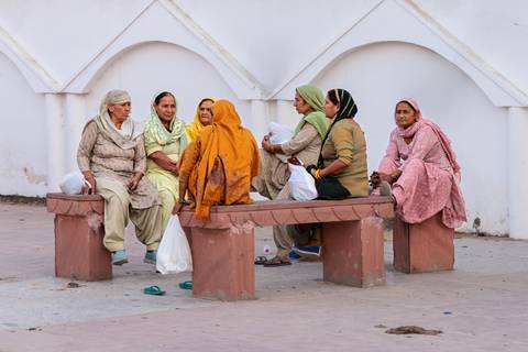 Group of elderly women seated and chatting on benches.