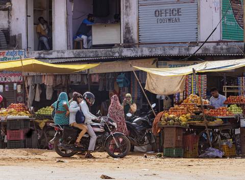       Motorbike carrying multiple people in a busy market area.
  