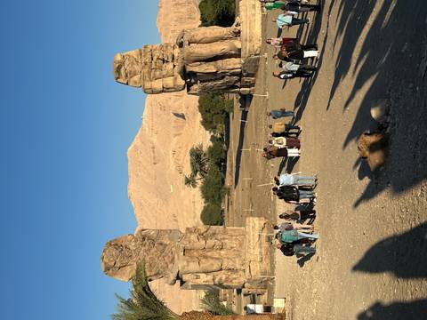       Group of tourists walking towards ancient colossal statues.
  