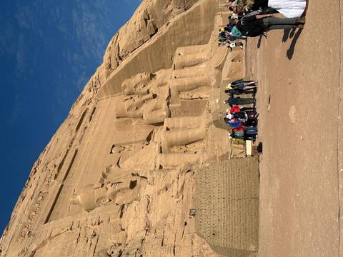       Tourists looking at rock-carved statues into a stone wall.
  