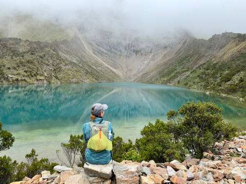 Hiker admiring a serene blue mountain lake surrounded by peaks.