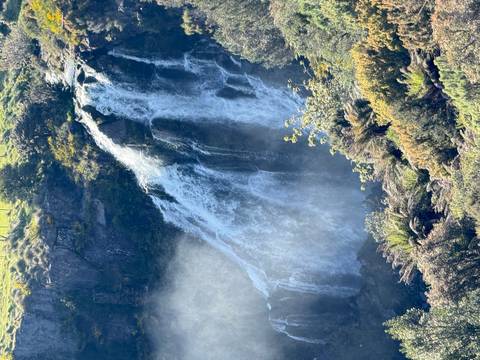       Waterfall cascading down rugged rocks into lush greenery.
  