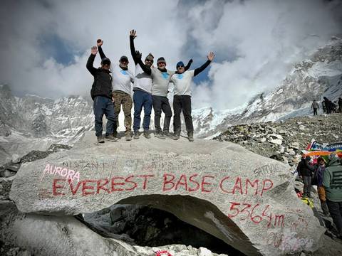       Group celebrating at the Everest Base Camp sign with mountains behind.
  