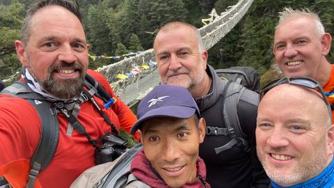       Group of hikers with a hanging bridge in the background.
  