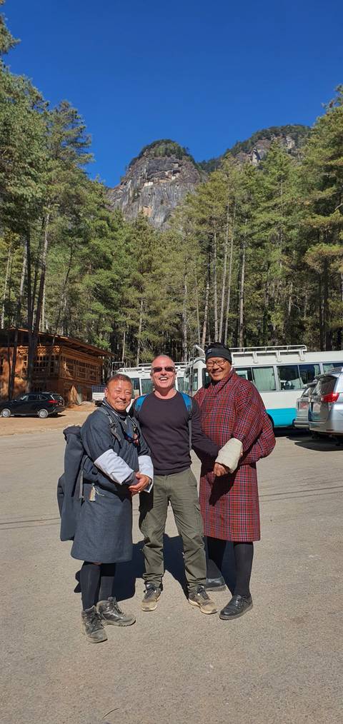       Group of people standing and smiling in an outdoor setting with trees.
  