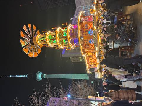       Night market scene with a tall illuminated decoration and TV tower.
  