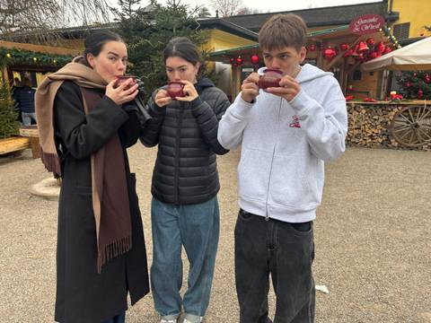       Three people enjoying hot drinks at a winter market.
  