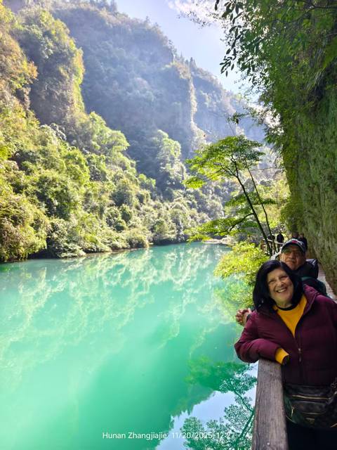 Two people smiling by a turquoise lake surrounded by lush greenery.