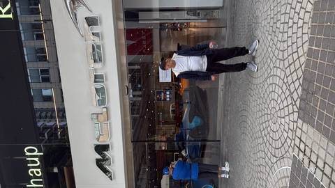 Person posing in front of a McLaren store with glass windows showing cars inside.