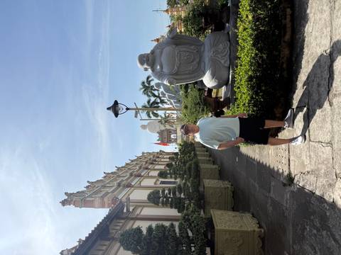 Person standing in courtyard with statues, cultural buildings, and a clear sky.