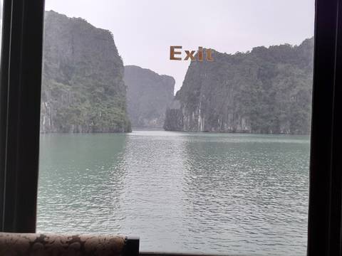 View through a window with 'exit' text, overlooking a bay with limestone cliffs.