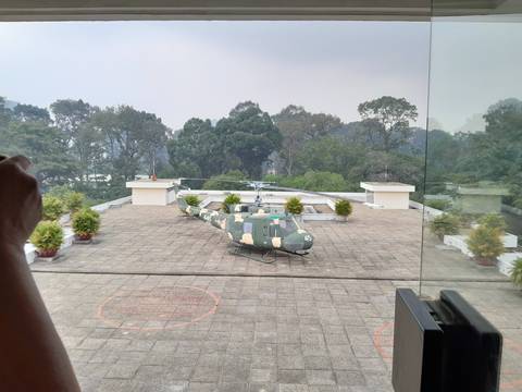 Military helicopter on a rooftop helipad surrounded by trees.
