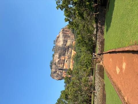      View of a large rock formation with a path and tourists.
  