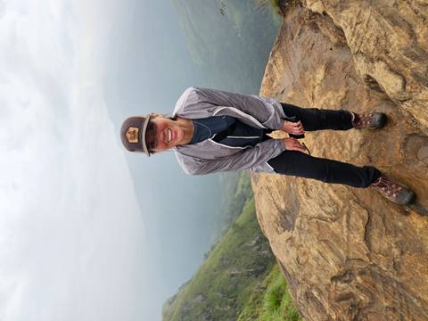 Person smiling on a rocky cliff with scenic views in the background.