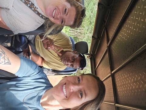       Group selfie of people inside a vehicle on safari.
  