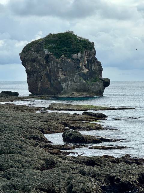 Large rock formation near a shoreline with clear blue water.
