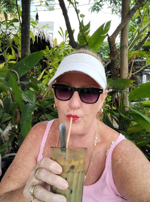       Woman drinking through a straw in a garden setting.
  
