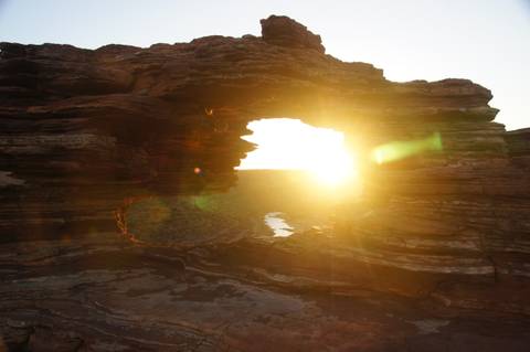 Sun setting through a rock formation, creating a dramatic light effect.