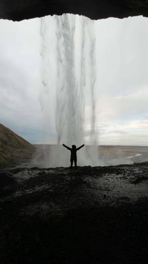 Person standing with arms wide open in front of a large waterfall.
