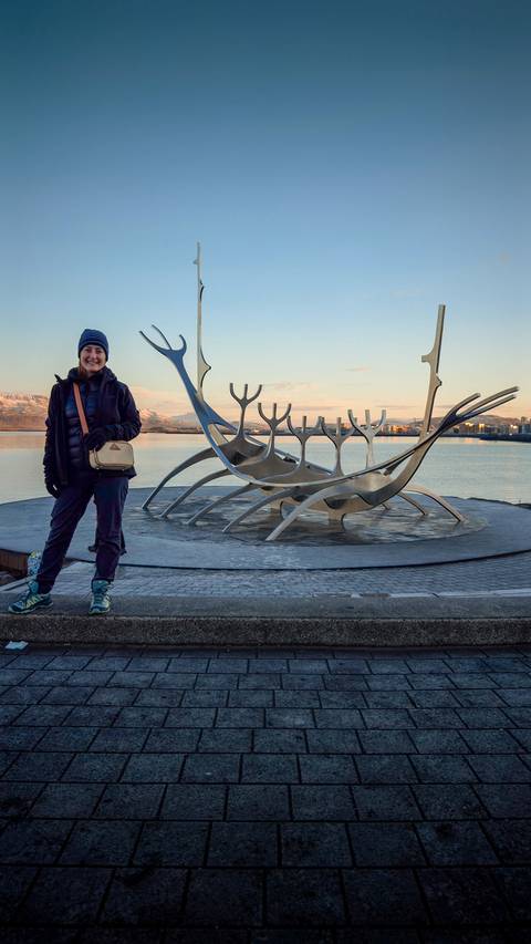 Woman posing in front of a modern sculpture by the water.