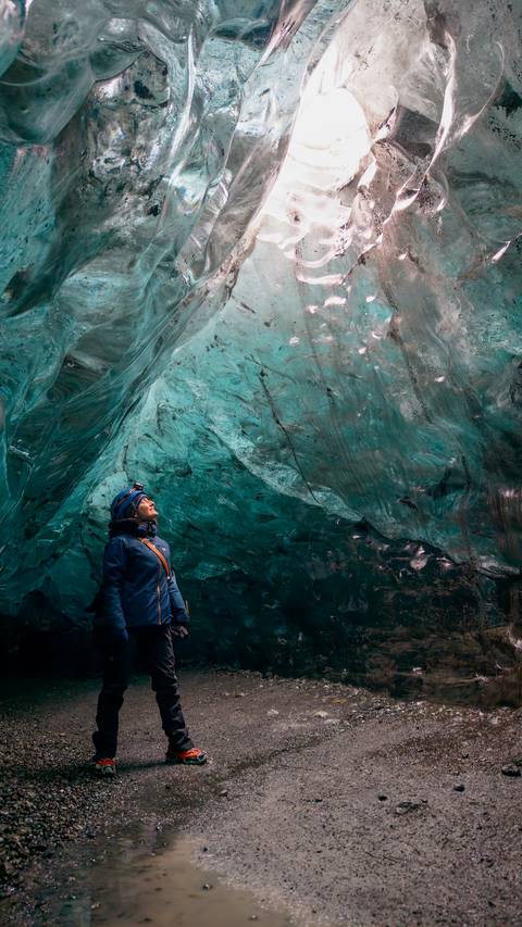      Person looking up at the icy blue ceiling of a cave.
  