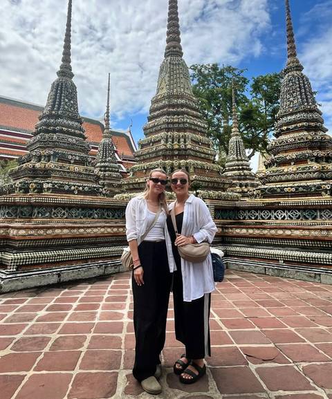 Two people posing in front of Wat Pho's ornate stupas.