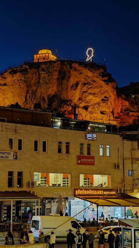 Building at night with glowing lights and a rugged backdrop.