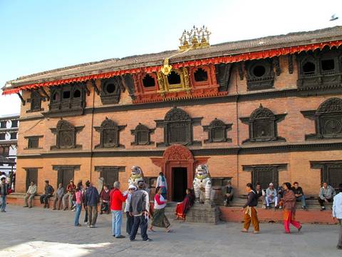 A brick temple adorned with sculptures with people gathered in front.