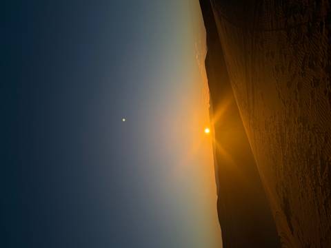       Sunset over sand dunes with a visible sun and clear sky.
  