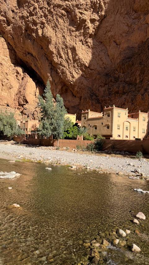       Traditional building along a dry riverbed with trees.
  
