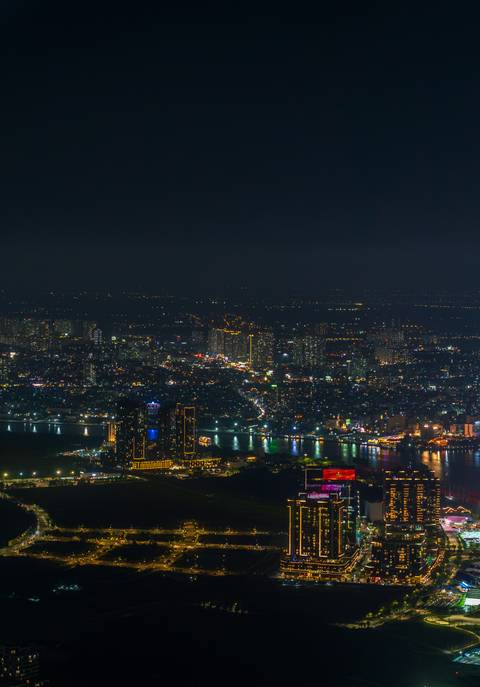       Aerial night view of a city with a brightly lit riverfront.
  