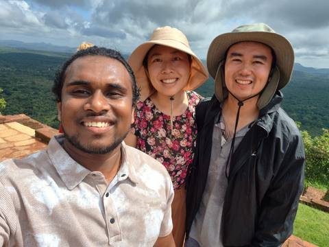 Three smiling people posing for a selfie with nature in the background.