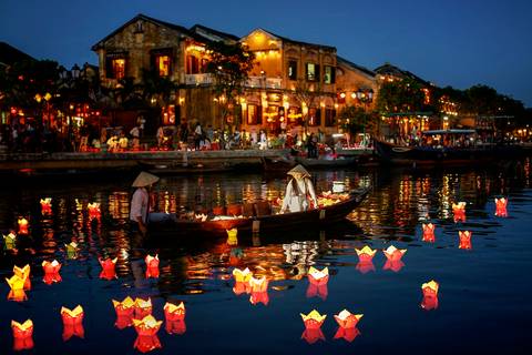 Evening scene of Hoi An with a boat on a river and illuminated lanterns.