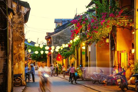       Vibrant street in Hoi An lit with lanterns and people on bikes.
  