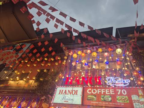       Street view in Hanoi with illuminated sign and decorations at dusk.
  