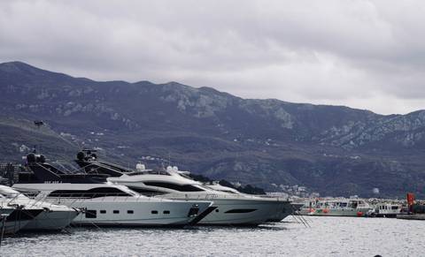 Yachts docked at a marina with mountains in the background.