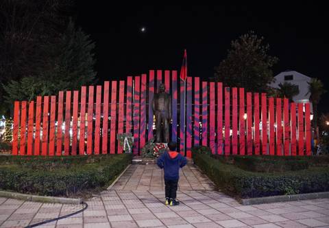 Child standing in front of a statue with a backdrop of flags.