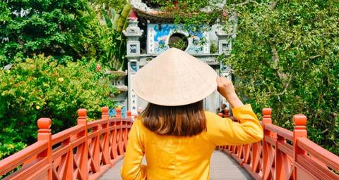       Person in traditional attire crossing a red bridge.
  